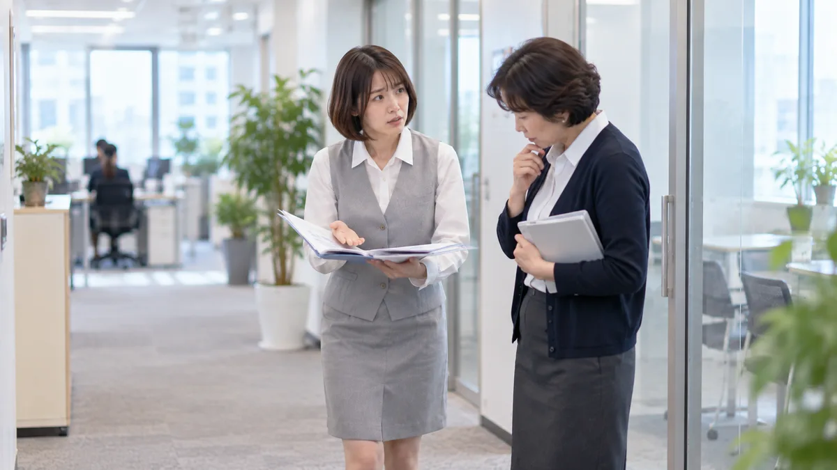 高圧的な女性に感情的に言い返さず、二つの仕事の資料を示しながら優先順位を落ち着いて確認している女性。