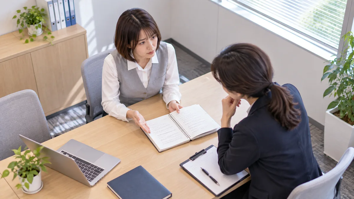高圧的な態度について記録したノートを開き、職場の相談相手に具体的な出来事を説明している女性。