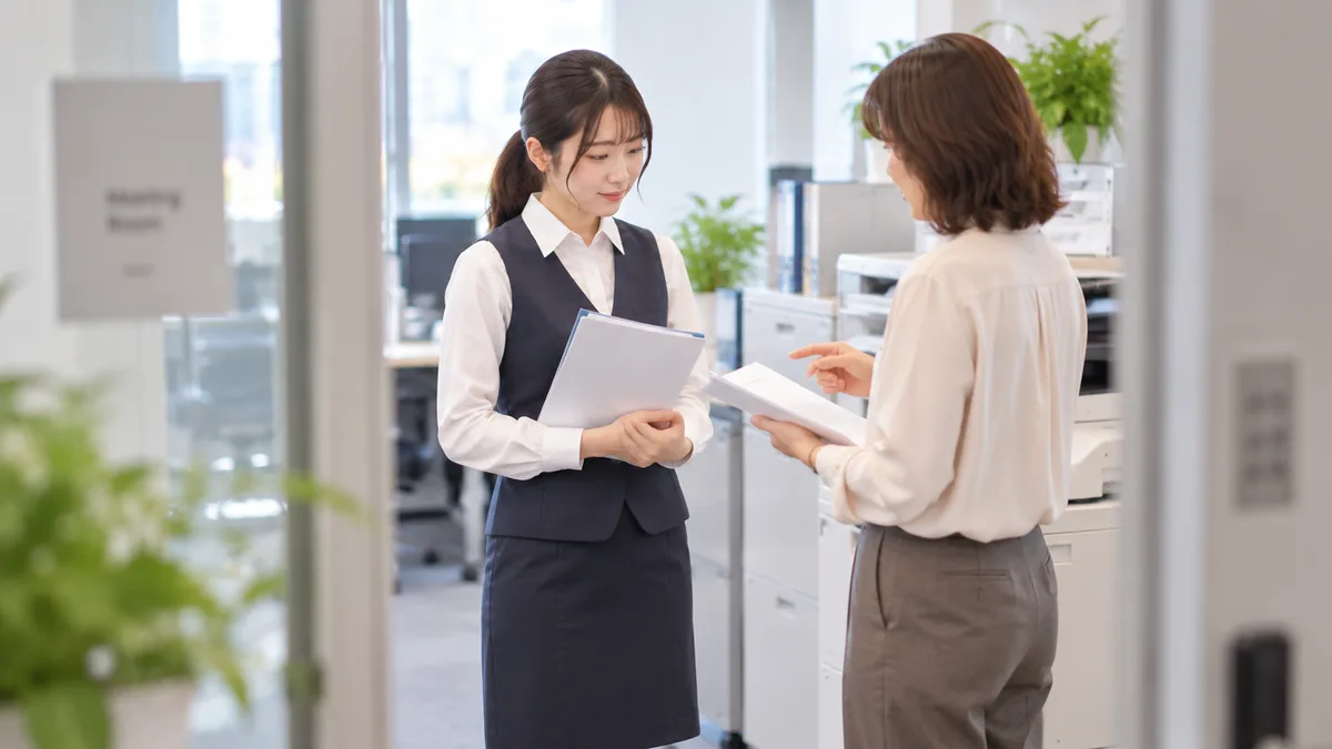 細かな指摘をする相手に感情的に反論せず、落ち着いて短く返事をしながら対応している職場の様子