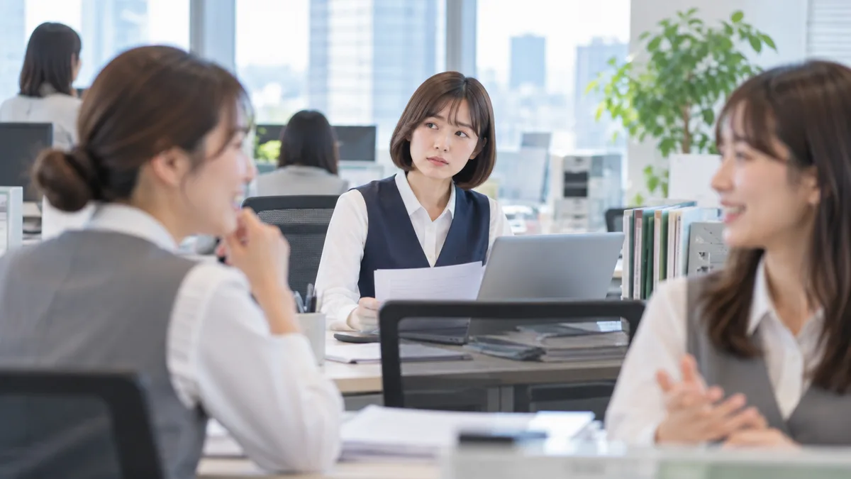 職場で周りの女性たちの様子を気にしながら、自分の席で少し疲れた表情をして仕事をしている女性